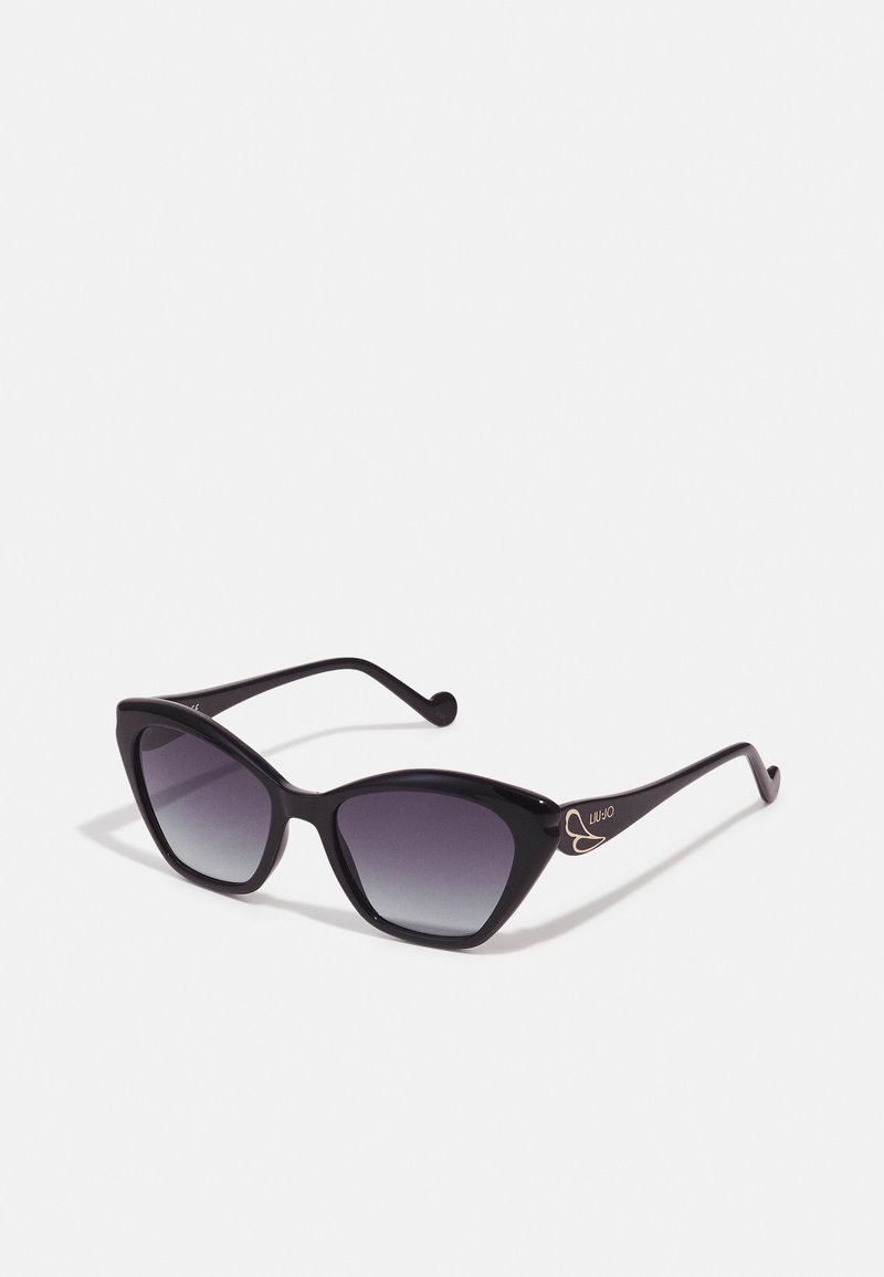 Lunettes de soleil noires en forme de chat avec verres dégradés. Monture en plastique audacieuse avec une texture lisse et un accent de logo doré sur la branche. Design élégant.
