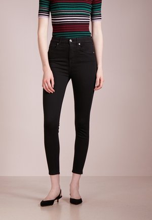 Person iført højtaljede sorte skinny jeans, kortærmet top med striber i mørkegrøn, bordeaux, hvid og sort, og sorte slingback-hæle.