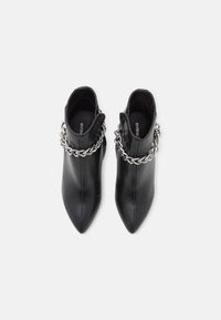 Botas de cuero negro hasta el tobillo con puntera puntiaguda, que cuentan con un acento de cadena plateada alrededor del tobillo y una cremallera lateral para el cierre.