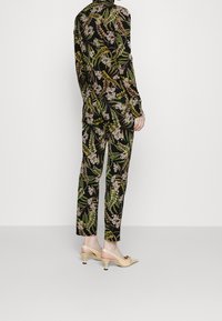 Tenue à motif floral avec un fond noir et un feuillage vert et blanc. Associée à des chaussures claires à petit talon.