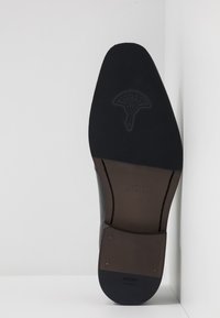 Suola di scarpa nera in pelle caratterizzata da un gomma testurizzata per una migliore aderenza, un logo inciso e un tacco in pelle marrone a contrasto con dettagli dorati.