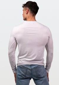 Jasnoszara koszula z długim rękawem o dopasowanym kroju, wykonana z gładkiego materiału, zestawiona z niebieskimi dżinsami. Prosty widok z tyłu, bez wzorów.