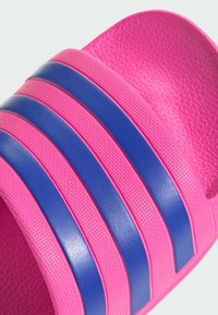 Pink slide sandal with textured finish, featuring three blue horizontal stripes across the upper. Designed for casual wear.