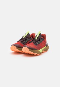 Rode en zwarte sportschoenen met een bovenwerk van mesh, groene accenten en een gestructureerde oranje zool. Beschikt over een gevoerde kraag en een vetersluiting.