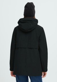 Chaqueta negra con capucha y cintura ajustada, de textura suave y corte a media longitud. Presenta un yugo trasero y mangas largas con puños abotonados.