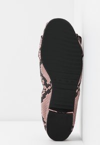 Zapato con estampado de serpiente en rosa y negro, con una superficie texturizada y una suela de goma negra sólida. Perfil lateral en ángulo contra un fondo blanco.