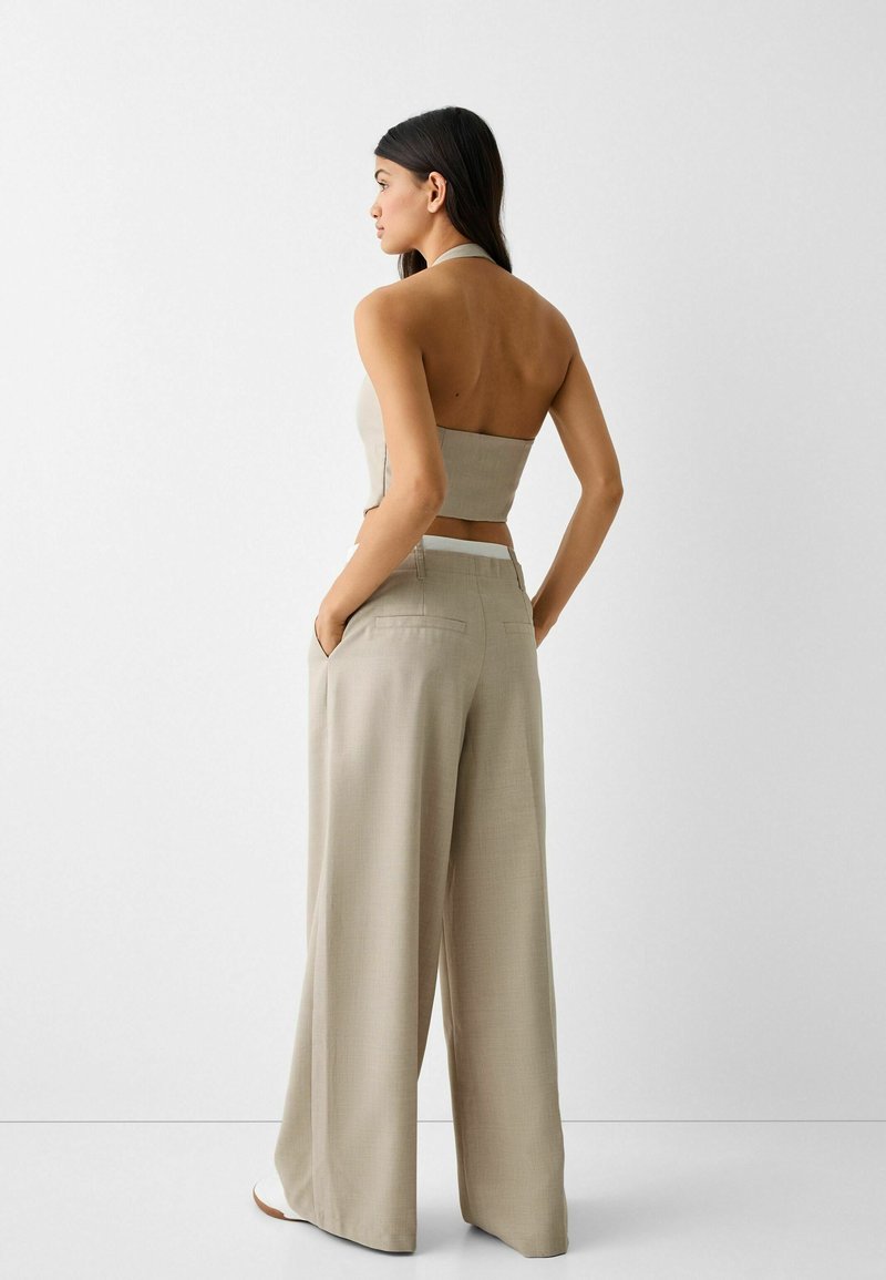 Beige cropped haltertop met een rechte snit, gecombineerd met hoge taille wijde broeken in dezelfde beige stof. Gladde textuur, minimalistisch ontwerp.