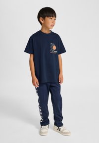 Donkerblauw katoenen T-shirt met een grafisch ontwerp op de borst, gecombineerd met donkerblauwe sweatpants met een witte zijstreep en sneakers.