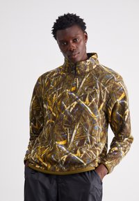 Fleece-pullover i brun med abstrakte gule og blå mønstre, høy krage, kvart-lukking, og myk tekstur.