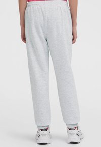 Persoon in lichtgrijze sweatpants met elastische boorden en witte sneakers, staand tegen een effen witte achtergrond.