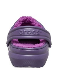 Bottines Crocs violettes avec semelle en caoutchouc texturée, doublure en peluche violette et sangle de talon ajustable. Présente le logo de la marque embossé sur le côté.