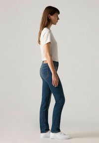 Camiseta de manga corta gris claro combinada con jeans skinny azul oscuro. Zapatillas blancas. Los jeans tienen bolsillos traseros y un detalle de etiqueta de la marca.