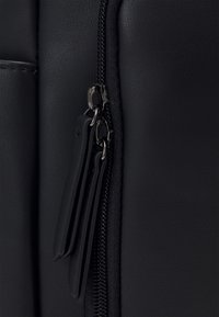 Détail d'un sac en cuir noir avec une fermeture éclair en métal argenté et une surface texturée, mettant en valeur des finitions lisses et mates.