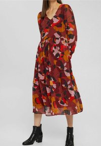 Långärmad klänning med V-ringning i blommönster i röda, rosa och bruna nyanser. Tillverkad av lätt tyg, med en utvikt fåll och lager-design. Bärs med svarta stövlar.
