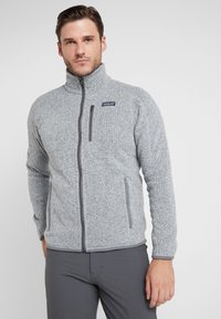 Gray fleece jacket with zip closure, high collar, and two side pockets. Features a textured pattern and a logo on the upper left chest.