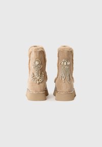 Beige ruskinn ankle støvler med pelskledde, med krystall anker og manet utsmykninger bak, samt teksturerte gummisåler.