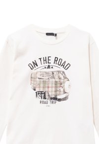 Camicia a maniche lunghe color crema con una stampa grafica che raffigura un furgone a quadri vintage e il testo "IN VIAGGIO PER IL PRIMO ROAD TRIP."