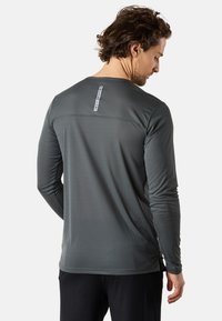 Langärmliges Performance-Shirt aus dunkelgrauem Stoff mit einem strukturierten Muster, ausgestattet mit einem Etikett im oberen Rückenbereich und Seitenschlitzen zur optimalen Passform.
