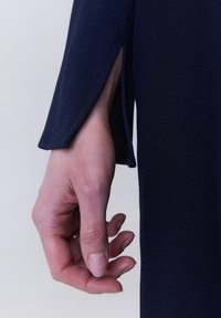 Dunkelmarineblauer Kleiderstoff mit glatter Textur und einem eleganten Schlitz am Ärmel. Eine Hand, die den Stoff greift, zeigt den Hautton und Details der Fingernägel.