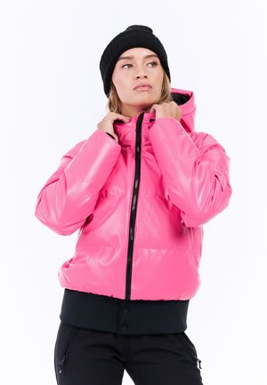 Roze pufferjack met een glanzende afwerking, een rits aan de voorkant en een zwarte ribbelzoom. Model draagt een zwarte gebreide beanie.