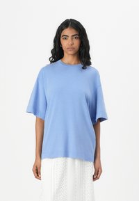 Lyseblå oversized t-skjorte i mykt stoff, med korte ermer og rund halslinje. Båret sammen med en hvit, teksturert skjørt.