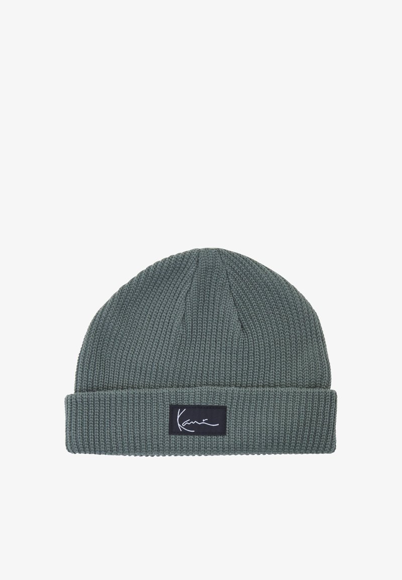 Bonnet tricoté gris avec un revers plié et une étiquette noire rectangulaire comportant un texte blanc en cursive à l’avant.