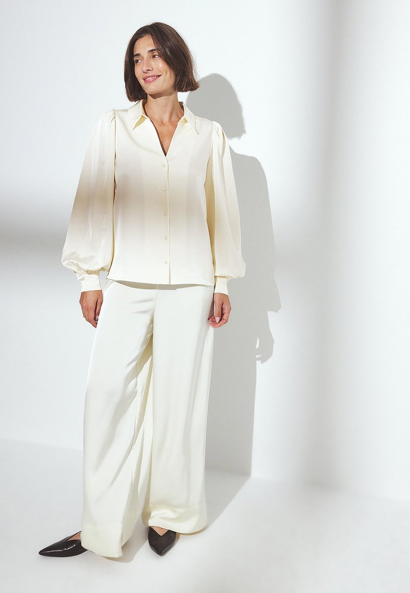 Cream-colored blouse with puffed sleeves and button front, paired with wide-leg cream pants; dark pointed flats complete the outfit.