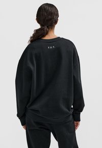 Svart oversized sweatshirt i mjukt tyg. Har sänkta axlar, ribbade muddar och en ryggtext med trycket "F.U.T." i en kontrasterande färg.