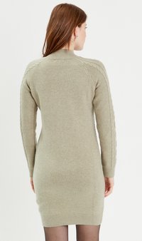 Sweter sukienka w stonowanej oliwkowej zieleni, z akcentami w warkocze wzdłuż rękawów i prążkowanymi mankietami, oferująca dopasowaną sylwetkę.