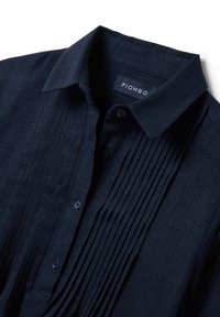 Camicia blu navy con colletto a bottoni e pieghe testurizzate sulla parte anteriore. Realizzata in tessuto leggero con una texture morbida.