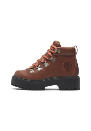 Brown leather hiking boot with orange laces, metallic eyelets, and a rubber sole. Features a textured surface and a logo on the side.