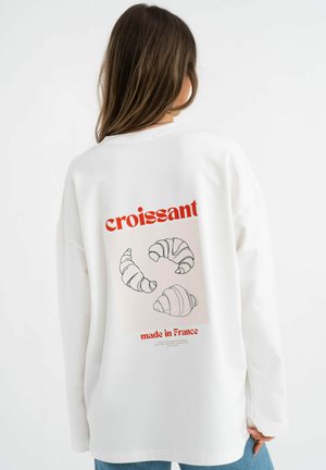 White sweatshirt featuring a printed design of croissants in a circular arrangement with the text "croissant" and "made in France" below.