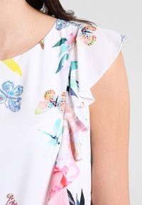 Blouse à fleurs en tissu léger, avec des imprimés de papillons et de fleurs multicolores, des manches volantées et un col rond.
