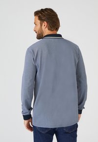 Grijze poloshirt met lange mouwen en een marineblauwe kraag, van een gestructureerde stof en contrasterende manchetten, gezien van achteren. Casual ontwerp dat geschikt is om in laagjes te dragen.