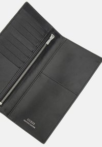 Billetera de cuero negro con bordes cosidos, cuenta con ranuras para tarjetas, un bolsillo con cremallera y el logotipo «GUESS GENUINE LEATHER» en relieve.