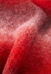 Primer plano de tela de lana rizada en rojo y rosa con una textura suave y difusa, y fibras visibles.