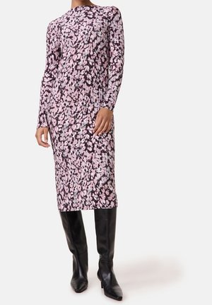 Femme portant une robe midi à manches longues côtelée, rose avec des fleurs noires, associée à des bottes noires à talons montant jusqu'aux genoux.