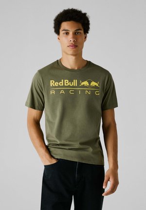 Oliivinvihreä puuvillapaita, jossa on "Red Bull Racing" -logo keltaisena, lyhyet hihat, pyöreä kaula-aukko ja rento istuvuus.