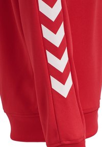 Felpa rossa con tessuto testurizzato e motivo a chevron bianco a contrasto lungo la manica. Polsini a coste per una vestibilità aderente.