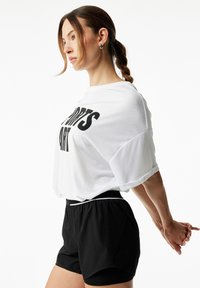 Biała koszula z krótkim rękawem z czarnym napisem, połączona z czarnymi szortami sportowymi z elastycznym pasem i białym wykończeniem na dolnej krawędzi.
