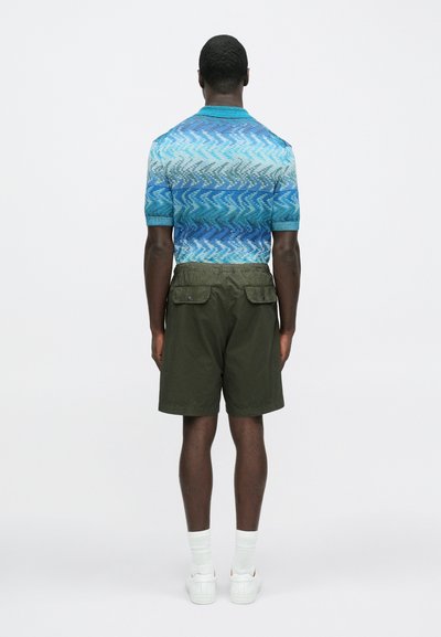 Modrý a zelený pletený polo triko s krátkými rukávy ve vzoru, doplněné o olivové šortky. Model má na sobě bílé tenisky a ponožky do poloviny lýtek.
