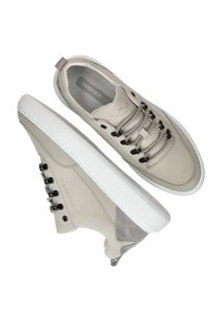Beige leren sneakers met een gladde en suède textuur, voorzien van zwarte veterogen en grijze veters, en een dikke witte rubberen zool.