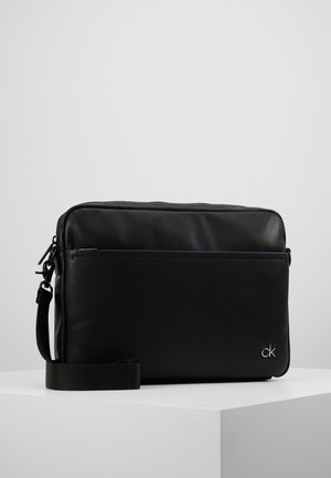 Sort skuldertaske i tekstureret læder med forrum, aftagelig rem og lille sølv "ck" logo i nederste højre hjørne.