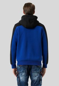 Blaues und schwarzes Kapuzensweatshirt mit glatter Textur. Verfügt über eine kontrastierende schwarze Kapuze und Schultereinsätze. Rippbündchen und -saum.