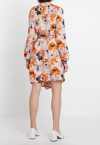 Blommig klänning i rosa, orange och svart; har långa ärmar, midja med bälte och knälång nederkant. Buren med vita klackskor med blockklack.