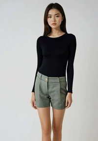 Haut noir à manches longues associé à un short à carreaux verts avec détails de boutons à la taille et coupe ajustée.