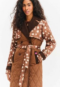Brązowy pikowany płaszcz z górną częścią przypominającą cętkowane futro, dużym kołnierzem, dwurzędowymi guzikami oraz paskiem do wiązania z kieszeniami.