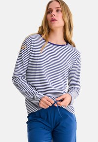 Gestreepte lange mouw top in wit en marineblauw, met een geribbelde textuur en een ronde hals. Gecombineerd met blauwe broek met trekkoord.