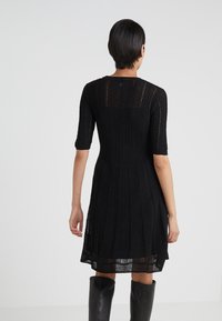 Abito nero in maglia con corpetto aderente, maniche corte e gonna a trapezio con un motivo a trama aperta e testurizzato.