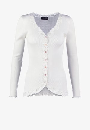 Gilet blanc à côtes avec un ourlet en dentelle festonnée, six boutons roses sur le devant et des manches longues. Tissu texturé avec une coupe ajustée.